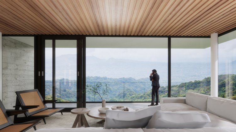 Man in black suit standing on balcony talking on phone with mountain landscape in the background.